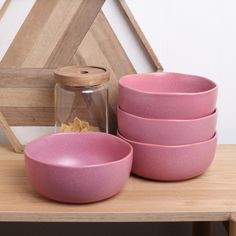 four pink bowls sitting on top of a wooden table next to a glass jar and vase