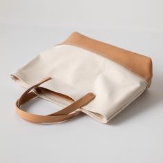 The Natural Canvas mini panel tote is a canvas and leather tote handmade in the KMM & Co. studio in Atlanta. Each one is meticulously crafted from heavyweight canvas (which is durable enough to stand up on its own) and gorgeous full-grain leather. Natural Canvas is an undyed cotton canvas, and the natural fibers have some subtle color variation that makes the canvas look slightly speckled. The Natural Canvas mini panel tote comes standard with Russet handles and a Natural Essex bottom panel. (To Beige Waxed Canvas Tote Bag, Beige Rectangular Duck Canvas Bag, Beige Duck Canvas Rectangular Bag, White Leather Canvas Bag With Top Carry Handle, Beige Waxed Canvas Bag With Leather Handles, Leather Canvas Tote Bag With Handles, Cream Coated Canvas Everyday Bag, Large Capacity Leather Canvas Bag In Cream, Beige Leather Canvas Bag With Top Carry Handle