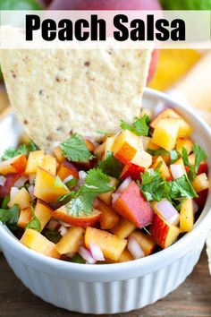 a white bowl filled with fruit and salsa next to tortilla chips on a wooden table