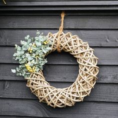 a wicker wreath hanging on the side of a wooden building with flowers in it