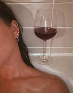 a woman laying in a bathtub next to a glass of wine