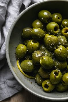 a bowl filled with green olives sitting on top of a wooden table next to a napkin