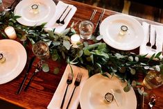 the table is set with white plates, silverware and greenery as well as candles