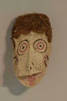 an old mask is hanging on the wall next to a white wall with a red and black face