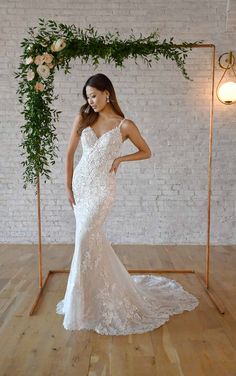 a woman standing in front of a white brick wall wearing a wedding dress with an open back