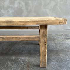 a wooden bench sitting on top of a cement floor next to a gray concrete wall