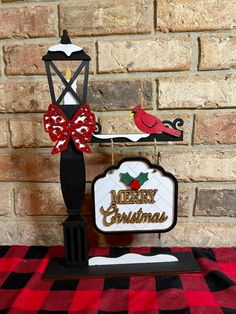 a christmas card holder on top of a red and black checkered table cloth next to a brick wall