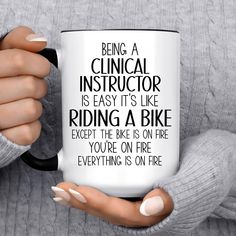 a woman holding a coffee mug that says being a medical instructor is easy it's like riding a bike except the bike is on fire you're on fire everything