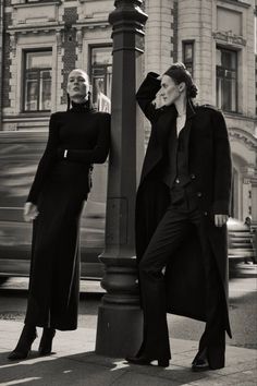 two women standing next to each other near a lamp post on the sidewalk in front of a building