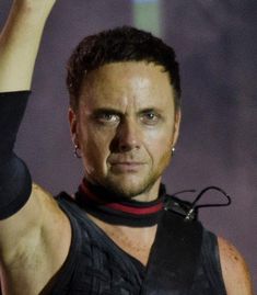 a man with his hand up in the air while wearing a black shirt and leather vest