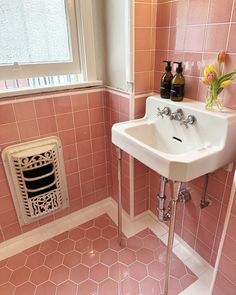 a bathroom with pink tiles and a white sink next to a radiator in the corner