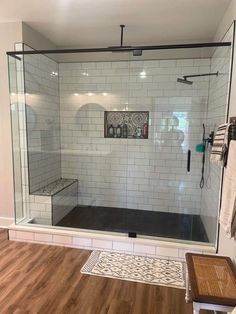 a walk in shower next to a wooden floor and white tiled walls with black accents