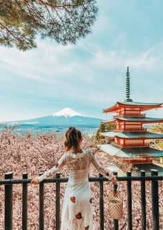 a woman standing on top of a balcony next to a tall building with a pagoda in the background