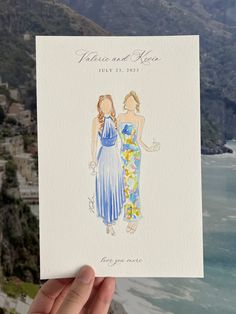 a hand holding up a card with two women in blue dresses