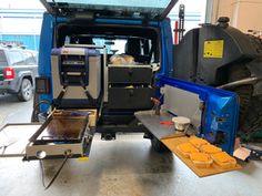 the back end of a blue truck with its doors open in a garage filled with other vehicles