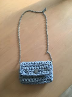 a crocheted blue purse sitting on top of a wooden table next to a chain