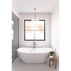 a white bath tub sitting under a window next to a wooden stool and table with potted plants