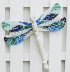 a blue and green dragonfly sitting on top of a white fence