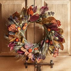 a wreath with dried flowers and leaves on a wooden door handle, in front of a wood paneled door