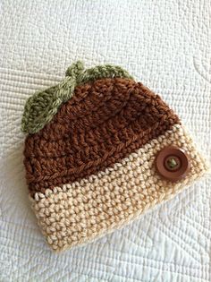 a crocheted hat is laying on top of a white bed with a brown button