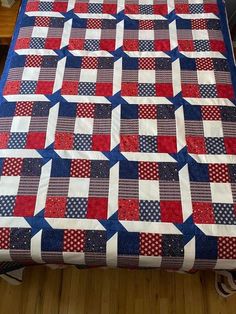 a red, white and blue quilt sitting on top of a wooden floor next to a table