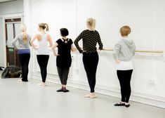 five women are standing in a row and looking at the wall with their backs turned