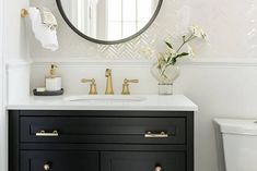 a white toilet sitting next to a bathroom sink under a round mirror on a wall