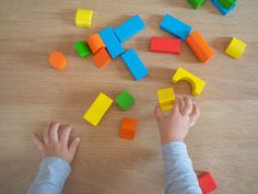 a child playing with colored blocks on a wooden table and holding their hands out to them