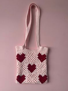 a crocheted bag with hearts on it hanging from a pink wall next to a pair of scissors