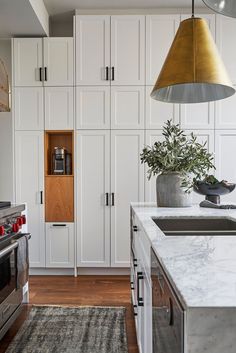 a kitchen with white cabinets and marble counter tops, gold pendant light hanging over the sink