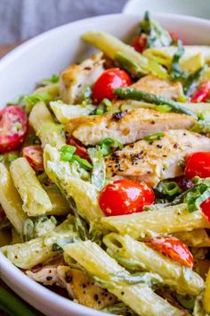 a white bowl filled with pasta and chicken topped with tomatoes, asparagus and cherry tomatoes