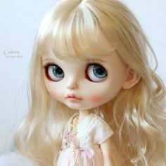 a close up of a doll with blonde hair and blue eyes wearing a pink dress