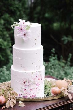 a three tiered white cake with pink flowers and leaves on the top is sitting on a table