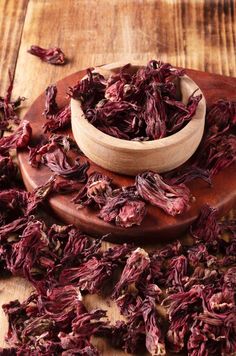 dried flower petals in a wooden bowl on a wood table next to a small spoon