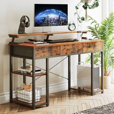 a desk with a computer on it in front of a window and a potted plant