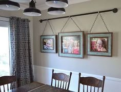 three framed pictures hang on the wall above a dining room table with four wooden chairs