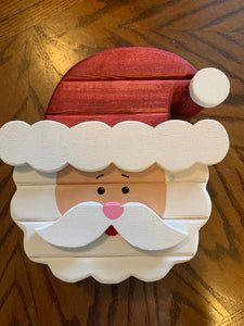 a cardboard santa clause with a red hat and mustache on it's head, sitting on a wooden table