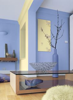 a glass table with a vase on it in front of a blue wall and wooden floor