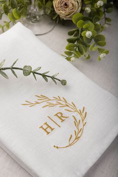 an embroidered napkin with the word h r written on it and flowers in vases behind it