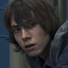 a close up of a person wearing a denim shirt and looking at the camera with a serious look on his face