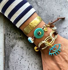 Elevate your accessory game with this stunning boho chic bracelet set. Featuring a blend of turquoise and gold tones, this set includes a handmade adjustable cord bracelet adorned with turquoise donuts and evil eye charms, paired with a hammered brass cuff. Perfect for adding a touch of bohemian elegance to any outfit. Ideal for summer fashion, festival wear, and unique gift ideas for her. Turquoise Hand Wrapped Bracelets For Festivals, Turquoise Bohemian Bracelets, Bohemian Turquoise Hand Wrapped Bracelets, Turquoise Bracelet Jewelry, Turquoise Bracelet Fashion Accessory, Handmade Bohemian Bracelets For Accessorizing, Bohemian Resizable Cuff Bracelet For Gift, Bohemian Resizable Cuff Bracelet As Gift, Adjustable Bohemian Brass Bracelets