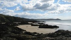 a sandy beach next to the ocean under a blue sky with white clouds in the background