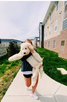 a woman walking down a sidewalk carrying a white dog in her arms and wearing tennis shoes