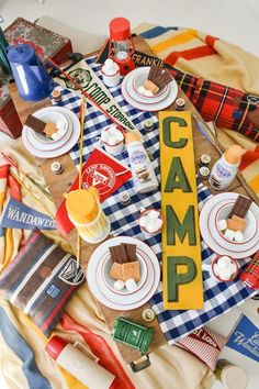 a camp sign is surrounded by food and camping items on a blanket that reads camp