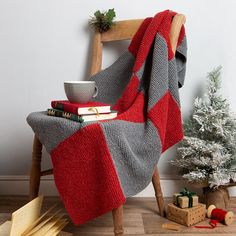 a red and grey blanket sitting on top of a wooden chair next to a christmas tree