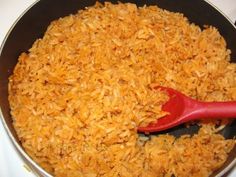 a red spatula in a skillet filled with rice on top of a stove