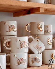 many white cups and saucers are stacked on a shelf with gold trimmings