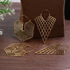 three pairs of gold earrings sitting on top of a wooden table next to a brown bag