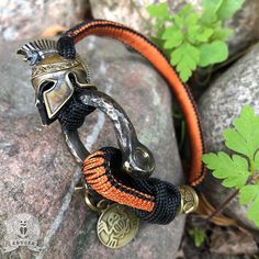 an orange and black bracelet with a spartan helmet on it sitting on top of a rock