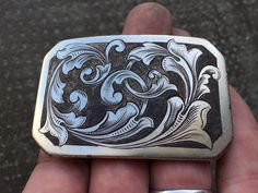 a person is holding a silver and black belt buckle in their left hand, with an intricate design on it